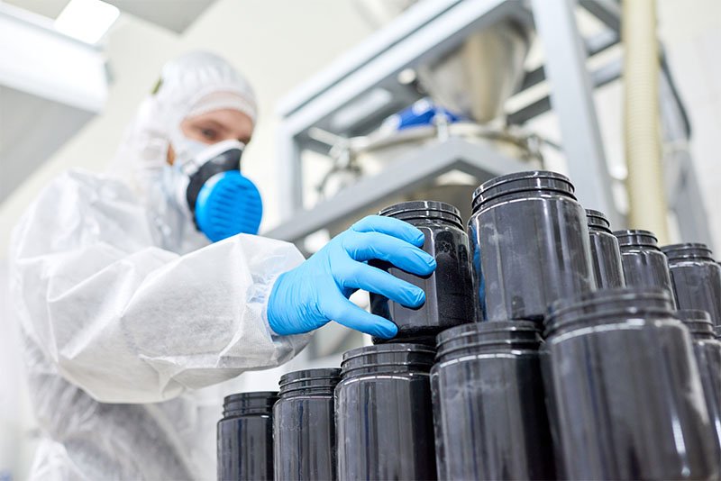 Factory employee inspecting plastic jar from manufacturing order of sports supplement, creatine, hmb, bcaa, amino acid or powdered vitamin. Sports nutrition production